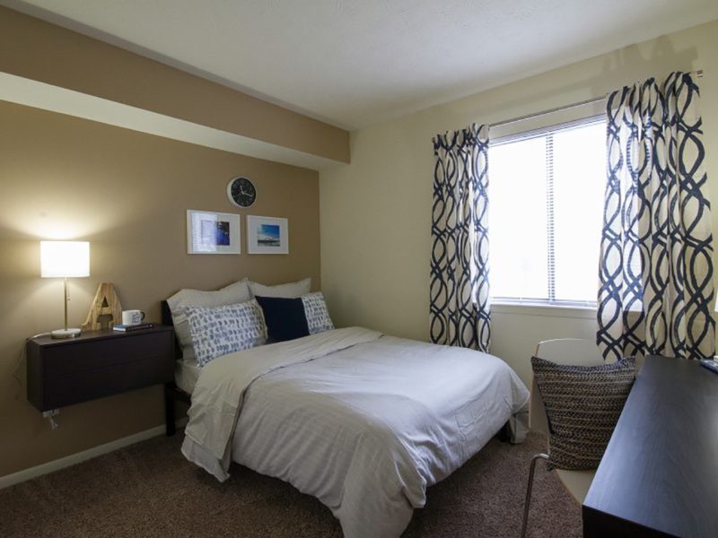 This image showcases the bedroom area featuring the caramel wall color, a mini working station, and cozy bedding.